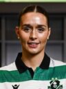Shamrock Rovers female player in team jersey, smiling, in stadium setting.
