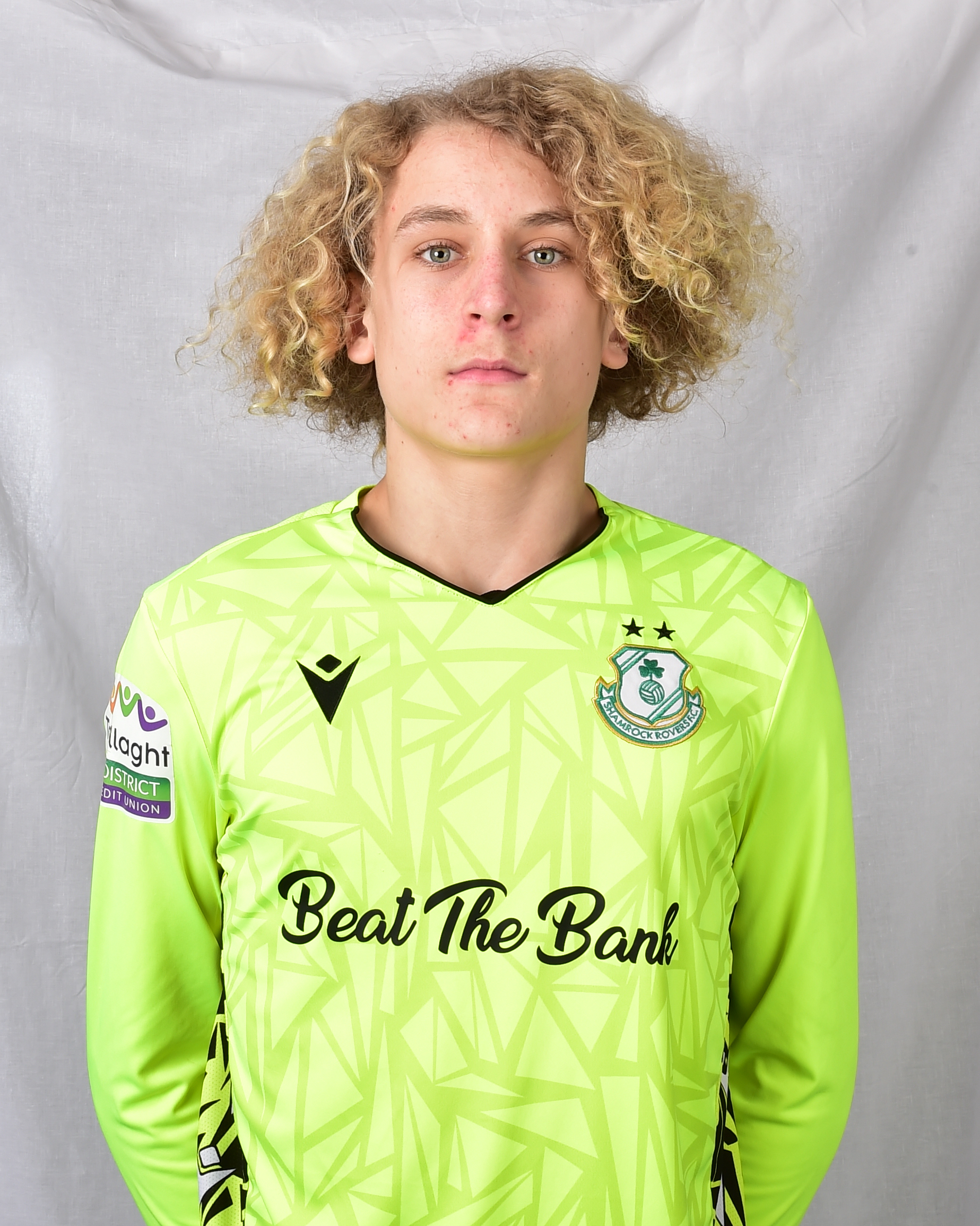 Shamrock Rovers football player wearing green kit, standing on grey background.