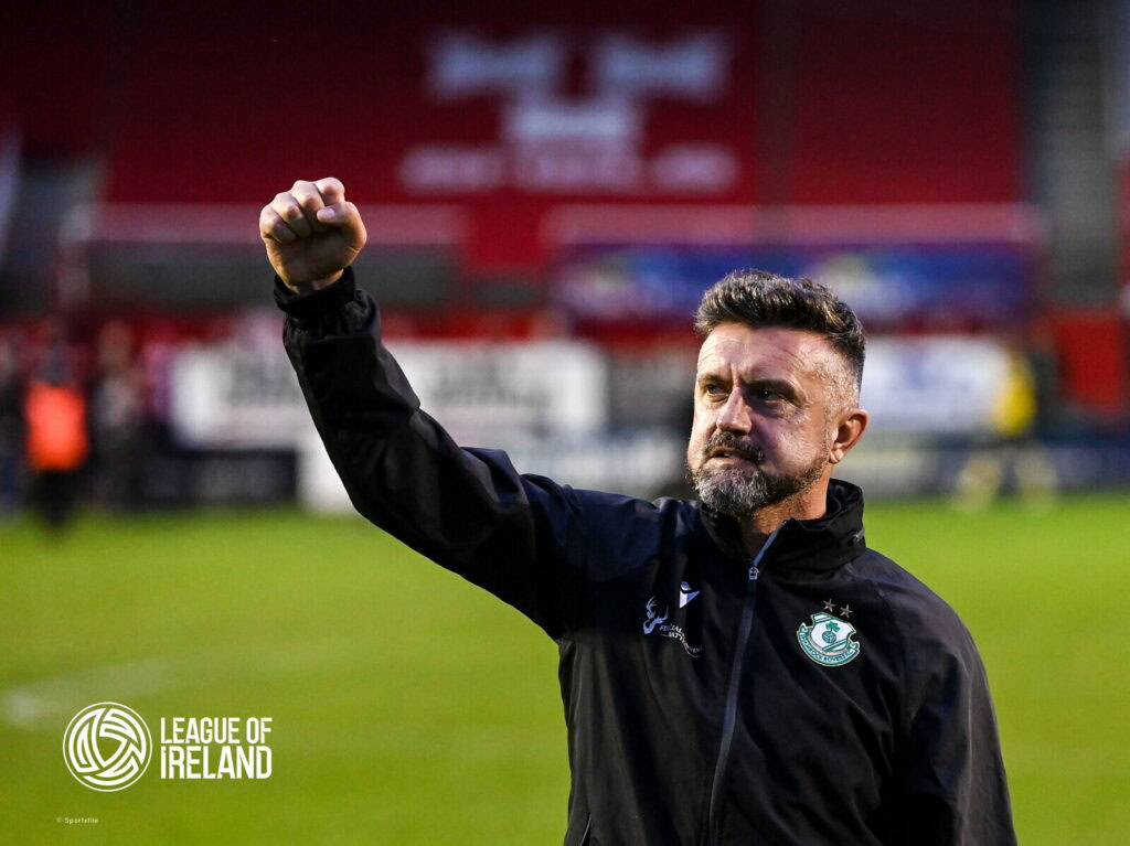 Celebrating Shamrock Rovers' victory, featuring a coach with the club badge, on a football pitch.