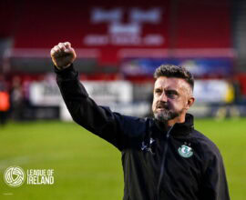 Celebrating Shamrock Rovers' victory, featuring a coach with the club badge, on a football pitch.