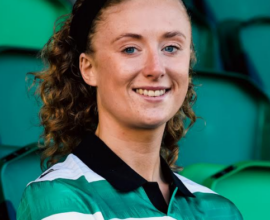 Female Shamrock Rovers footballer smiling in team kit at stadium.