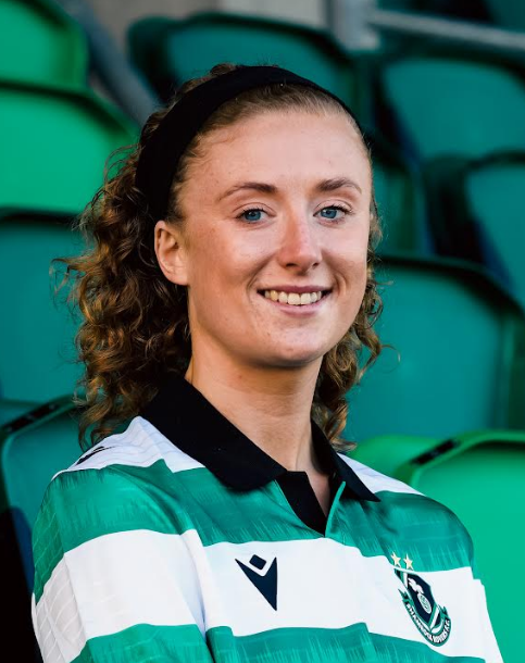 Female Shamrock Rovers footballer smiling in team kit at stadium.