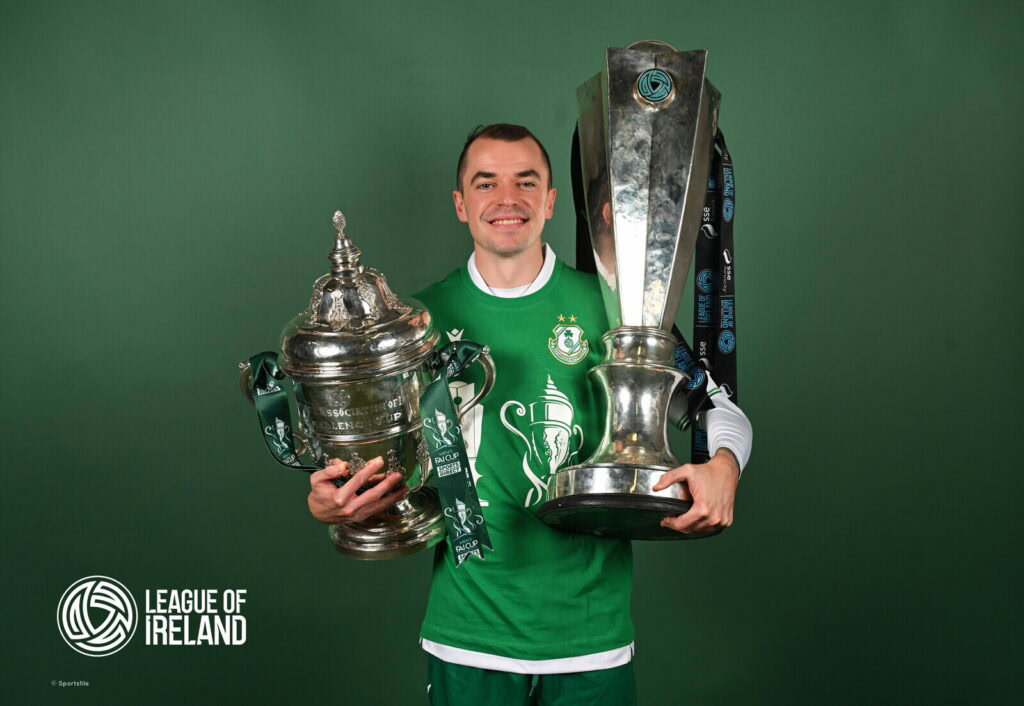 1. Irish football player holding League of Ireland trophies, celebrating victory.