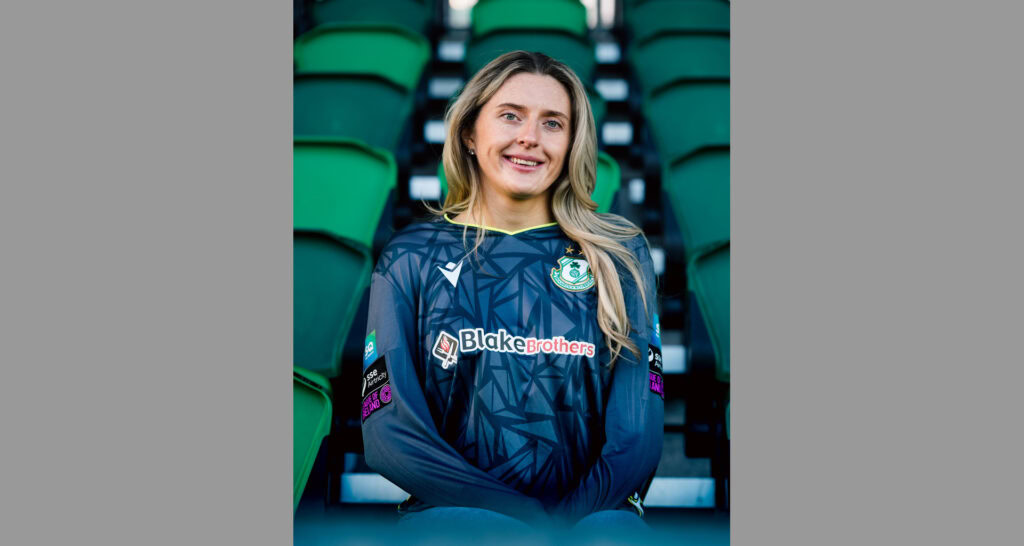 Shamrock Rovers female football player in club jersey at stadium seats.
