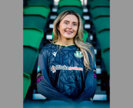 Shamrock Rovers female football player in club jersey at stadium seats.