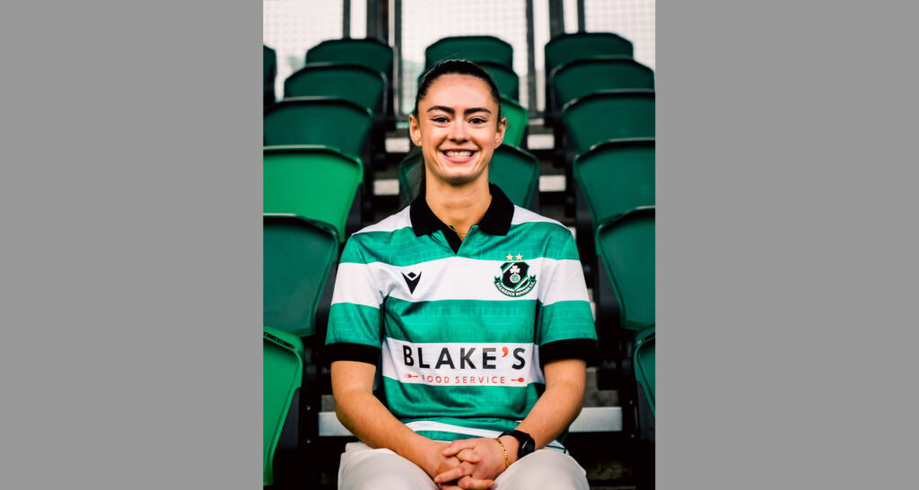 Woman wearing Shamrock Rovers football kit, smiling at stadium.