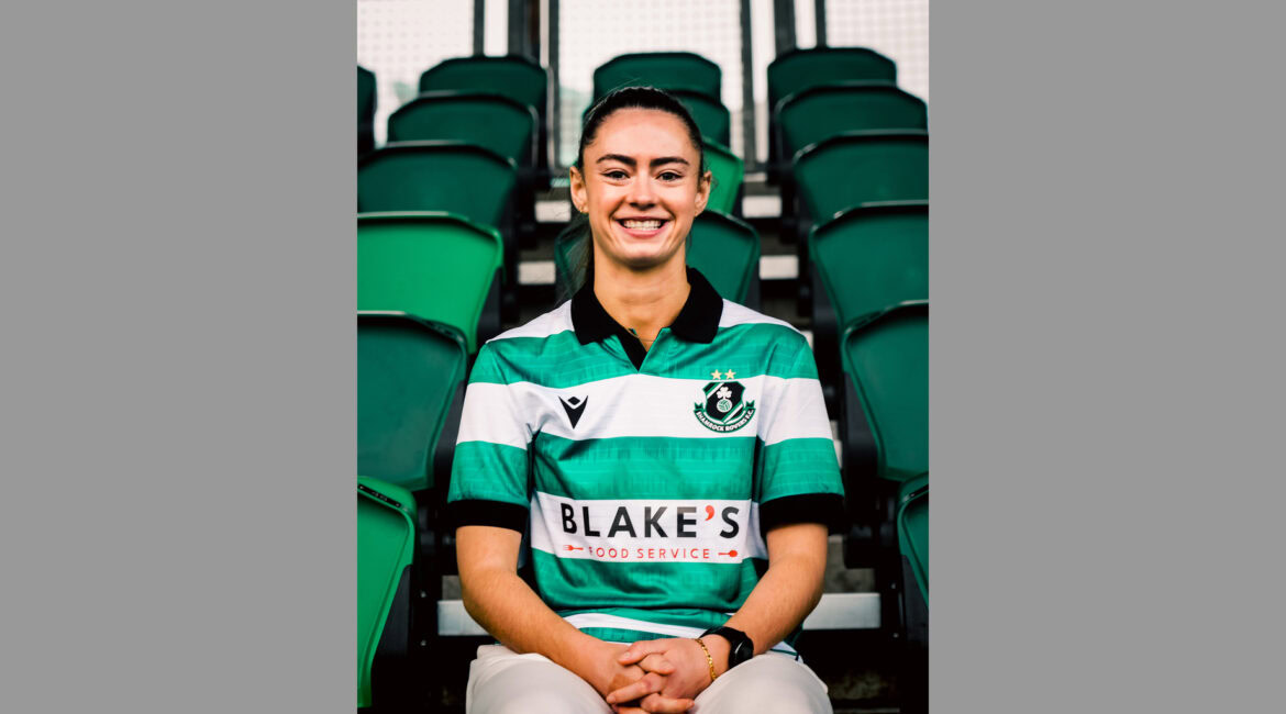 Woman wearing Shamrock Rovers football kit, smiling at stadium.