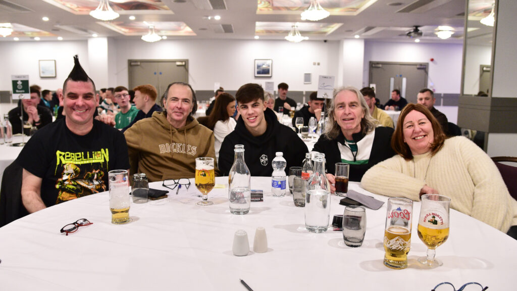 Happy people at table with drinks, Shamrock Rovers team fans, celebrating victory, Irish football supporters, indoor event.