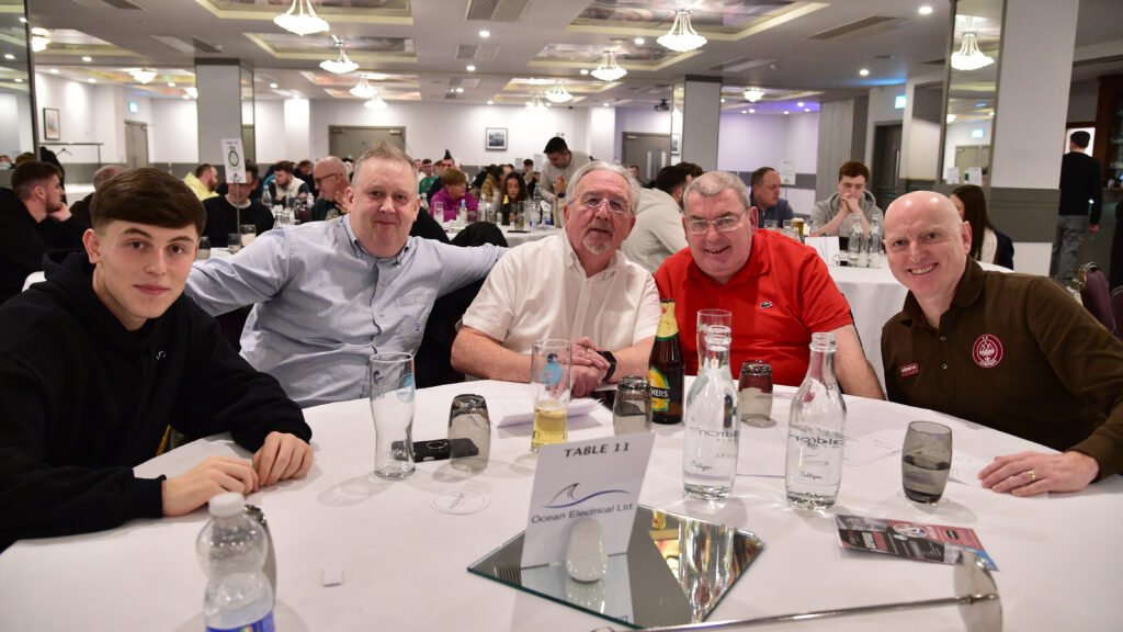 Brightly lit football fan event with Shamrock Rovers supporters enjoying a meal together at a formal gathering.