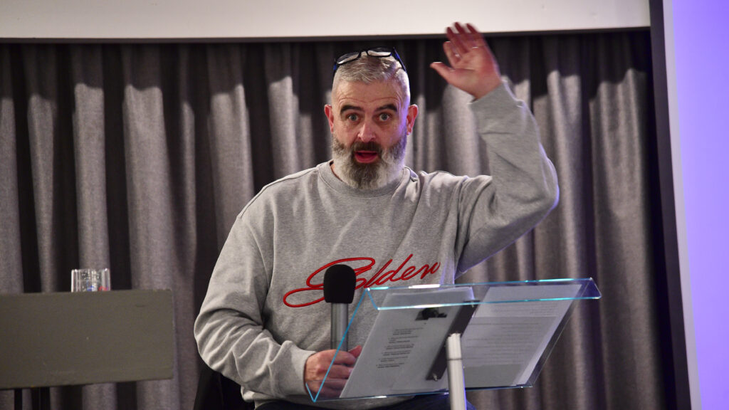 Male speaker at Shamrock Rovers event holding microphone, addressing audience.