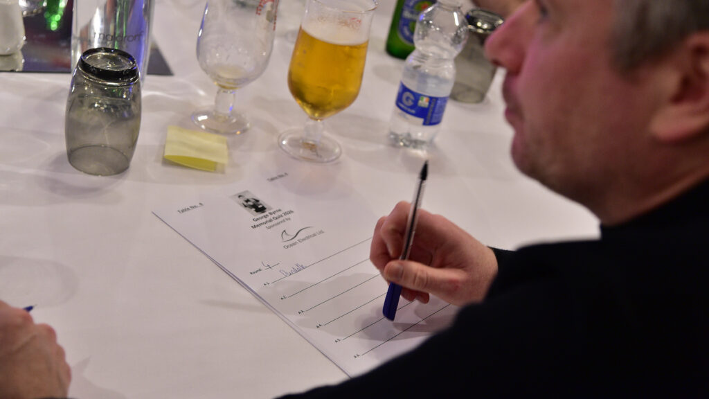 Football team player signing at a formal event, with drinks on the table.