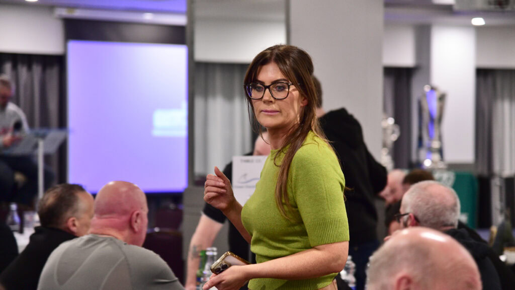 1. Female at Shamrock Rovers fan event, wearing green top, holding phone in a lively stadium atmosphere.