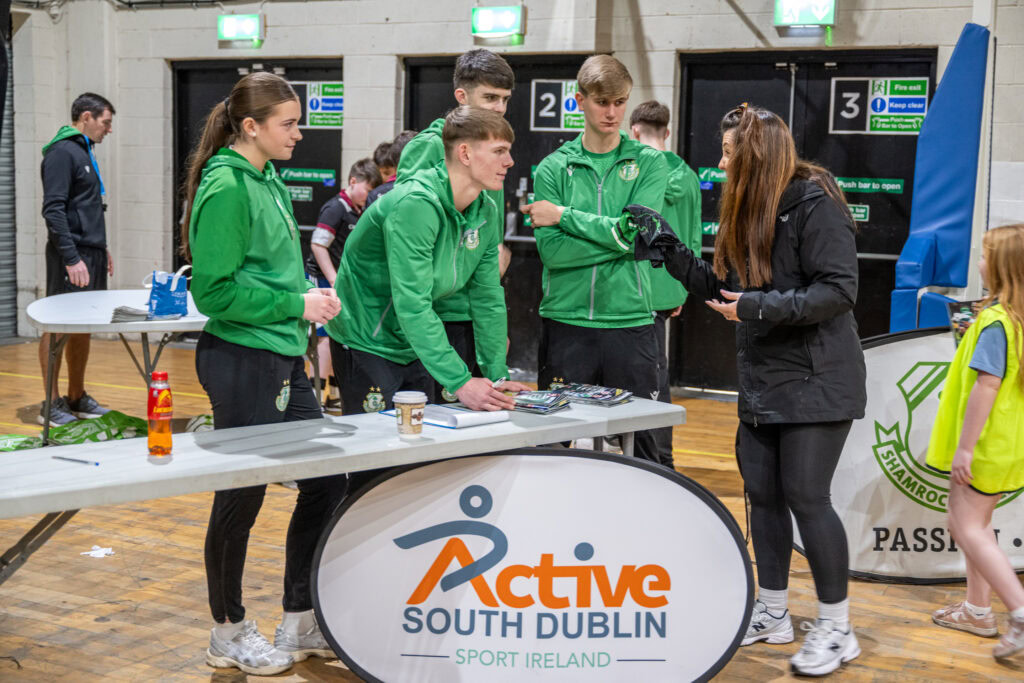 Shamrock Rovers football team signing autographs at indoor event in green kits.
