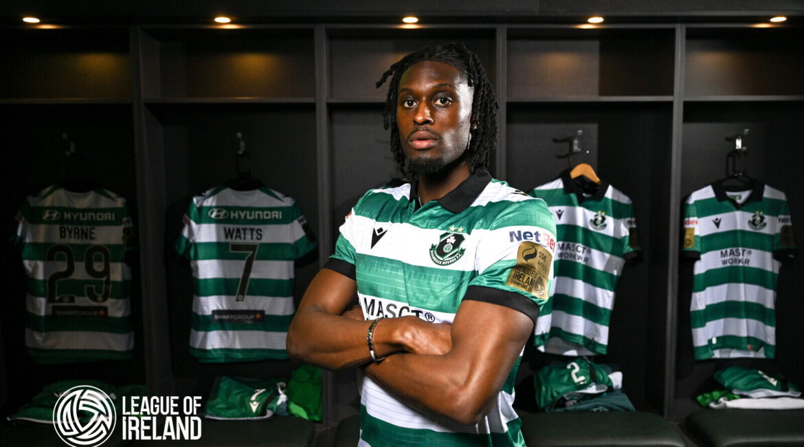 Shamrock Rovers player in locker room with team jerseys behind him.