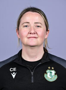Shamrock Rovers female coach in team jacket with club crest, smiling confidently.