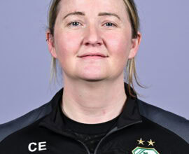 Shamrock Rovers female coach in team jacket with club crest, smiling confidently.