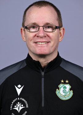 Shamrock Rovers coach smiling in team jacket with club crest, close-up portrait.