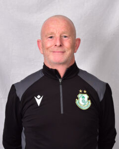 Shamrock Rovers coach in team gear, smiling, standing against a neutral background.