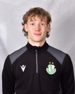Young Shamrock Rovers player in team training kit, smiling at camera.