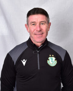 Shamrock Rovers coach in team gear, smiling, standing against a plain background.