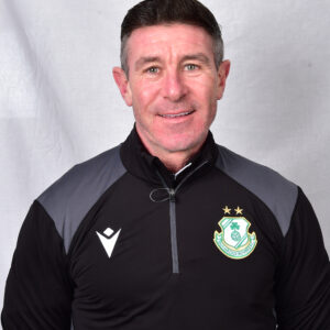 Shamrock Rovers coach in team gear, smiling, standing against a plain background.