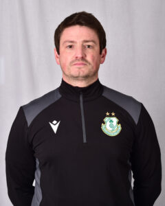 Shamrock Rovers coach in team training gear, standing confidently in front of a plain background.