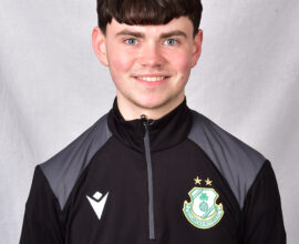 Young Shamrock Rovers player in team training jacket smiling at camera.