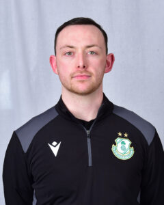 Shamrock Rovers football player in team kit with club crest, facing forward.