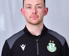 Shamrock Rovers football player in team kit with club crest, facing forward.