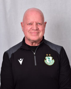 Shamrock Rovers coach in team gear, smiling, standing against a neutral background.