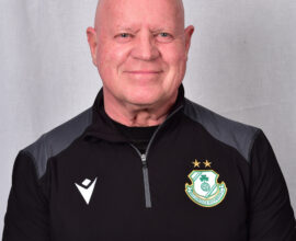 Shamrock Rovers coach in team gear, smiling, standing against a neutral background.