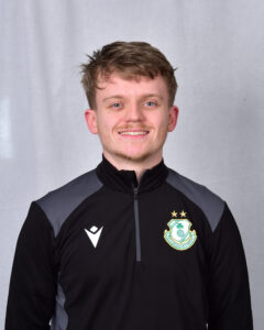 Shamrock Rovers football player smiling in team kit with club crest, standing against grey backgroun.
