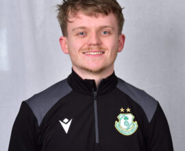 Shamrock Rovers football player smiling in team kit with club crest, standing against grey backgroun.