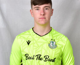 Young Shamrock Rovers goalkeeper in bright green jersey, facing forward.