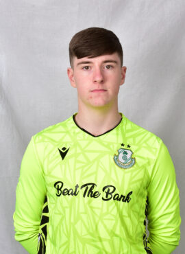 Young Shamrock Rovers goalkeeper in bright green jersey, facing forward.