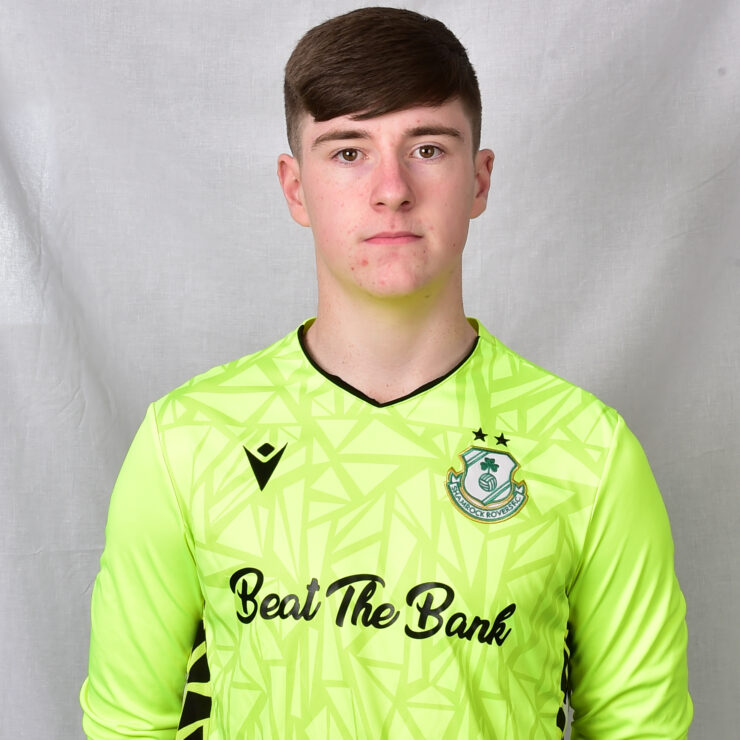 Young Shamrock Rovers goalkeeper in bright green jersey, facing forward.