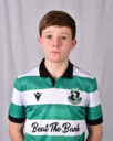 Young Shamrock Rovers player in green and white jersey, standing indoors.