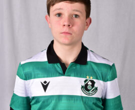 Young Shamrock Rovers player in green and white jersey, standing indoors.