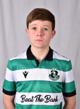 Young Shamrock Rovers player in green and white jersey, standing indoors.