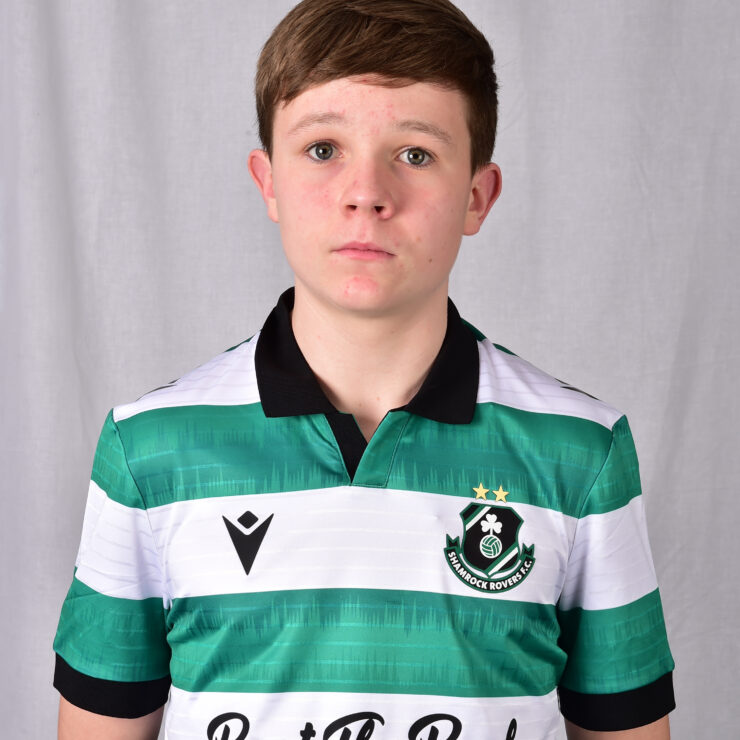 Young Shamrock Rovers player in green and white jersey, standing indoors.