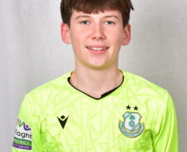 Young Shamrock Rovers player in bright green jersey smiling at camera.