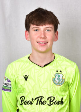 Young Shamrock Rovers player in bright green jersey smiling at camera.