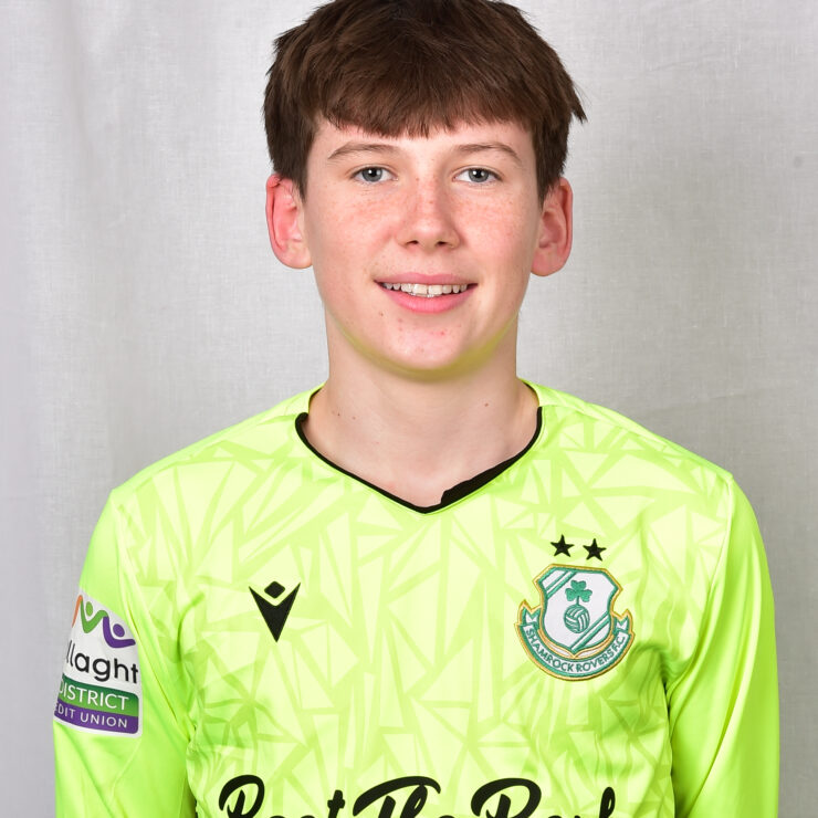 Young Shamrock Rovers player in bright green jersey smiling at camera.