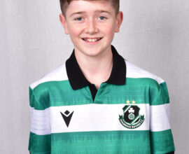 Young Shamrock Rovers player in team jersey smiling.