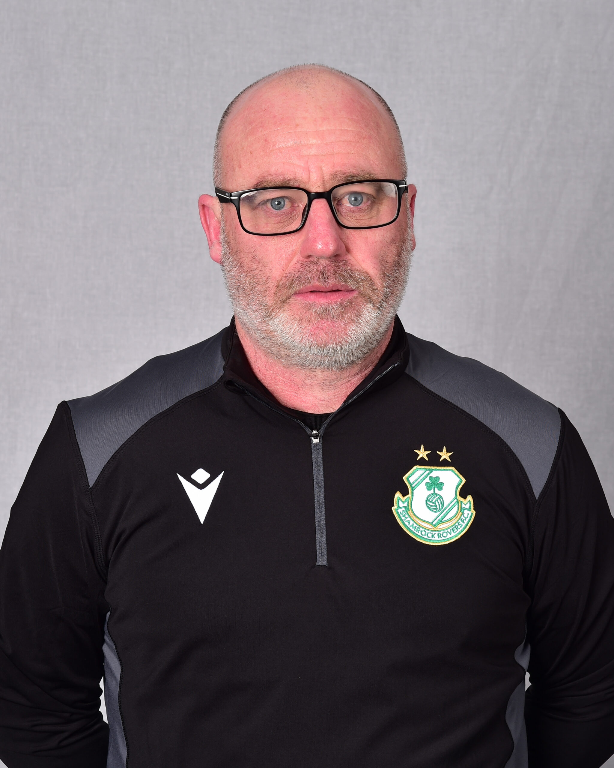 Shamrock Rovers coach in team jacket with club crest and glasses.