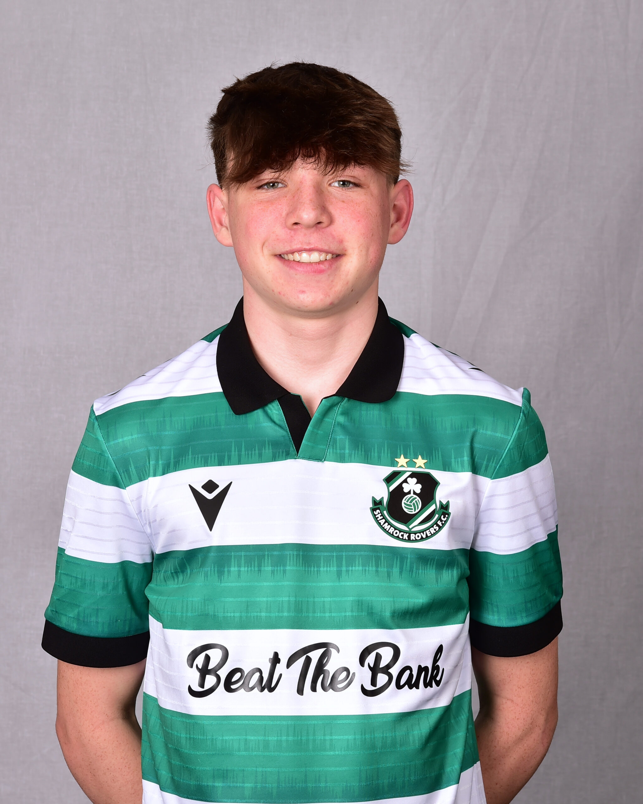 Young Shamrock Rovers football player in green and white kit smiling at camera.