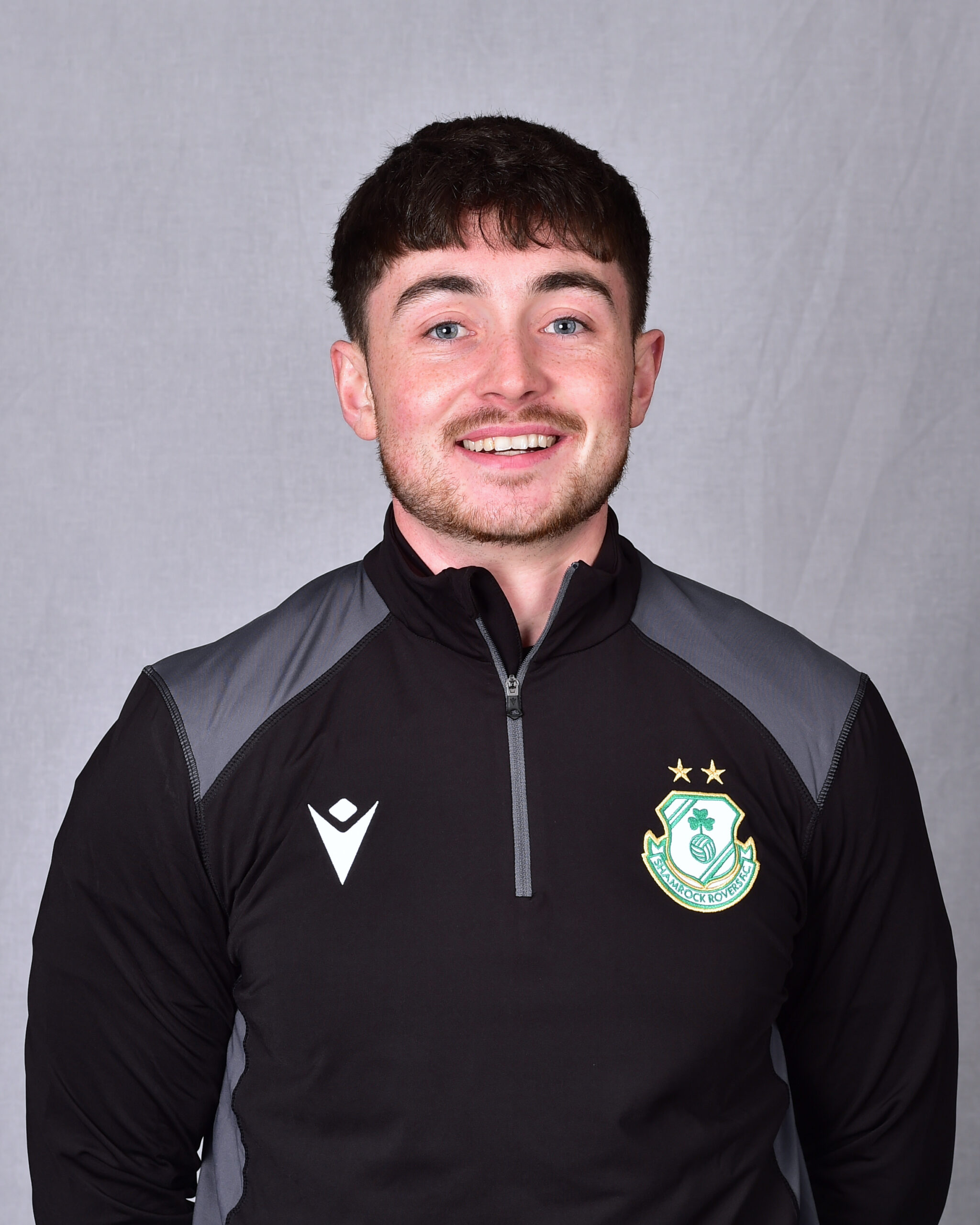 Shamrock Rovers football player in team kit smiling at camera.