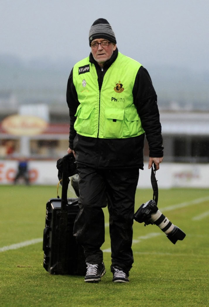 Shamrock Rovers staff member walking on the football pitch with camera and equipment.