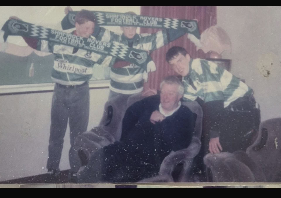 Group of Shamrock Rovers fans with scarves celebrating victory indoors.