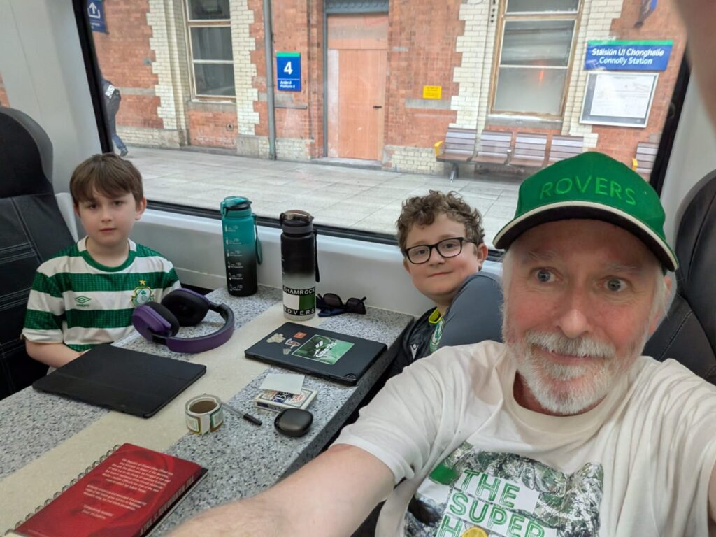 Shamrock Rovers fans, including children and an adult, sitting on a bus with team merchandise.